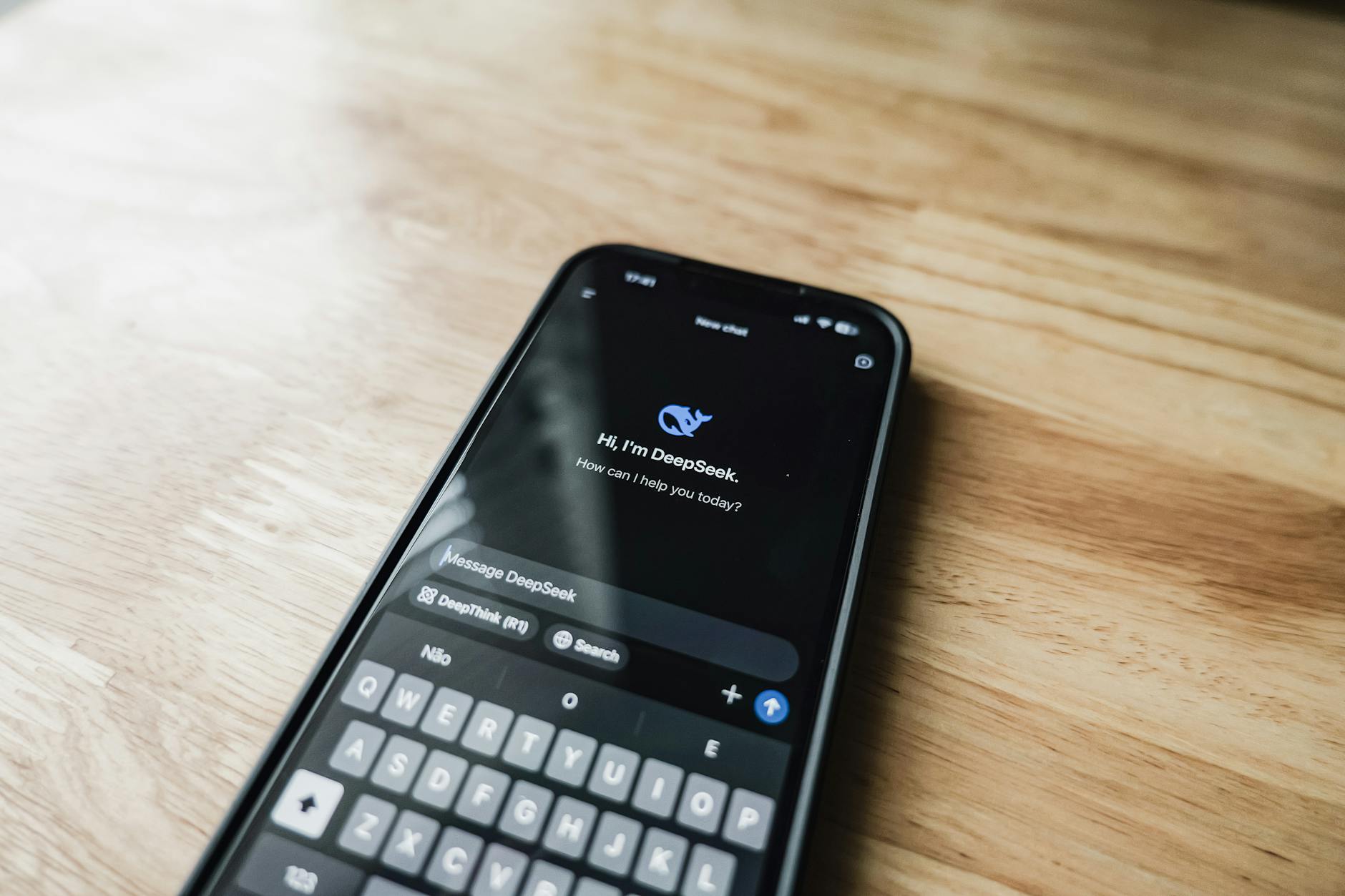 Smartfon z otwartym czatem AI DeepSeek leżący na drewnianym stole