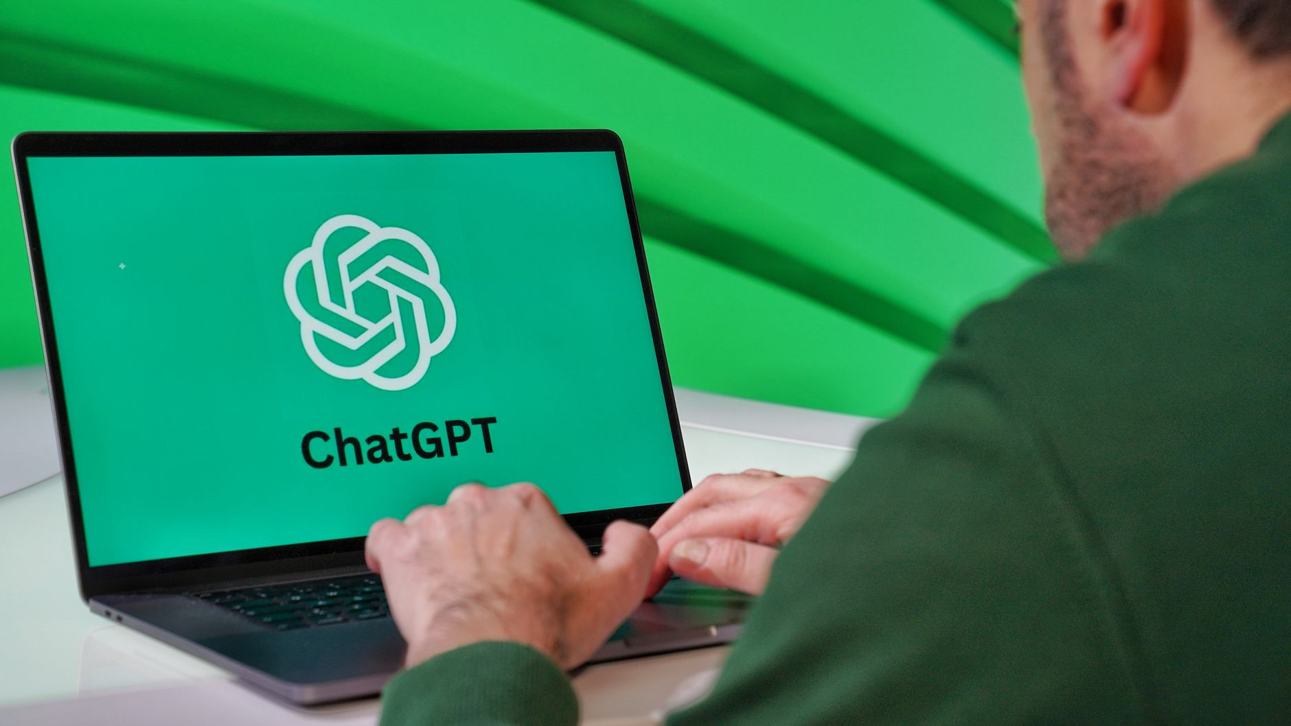 Osoba pisząca na laptopie z logo ChatGPT na zielonym tle